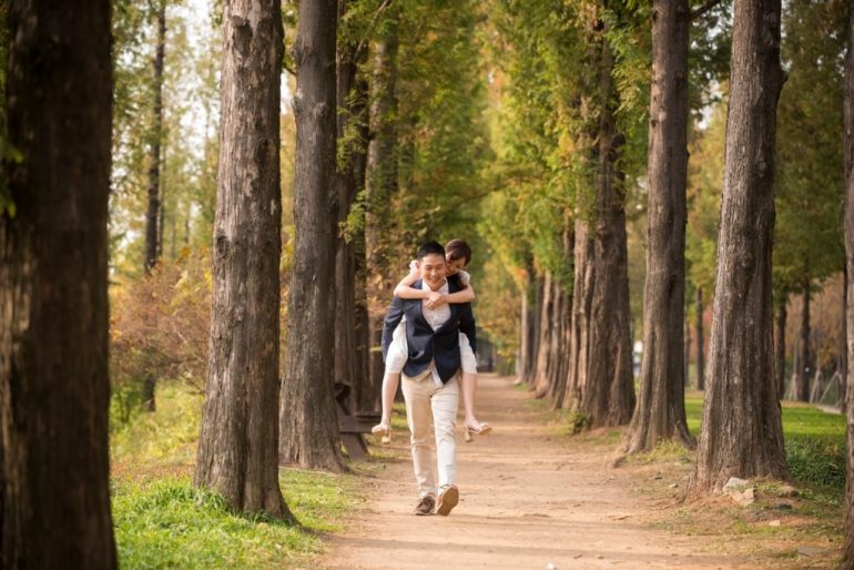 bride riding on back of groom walking down forest