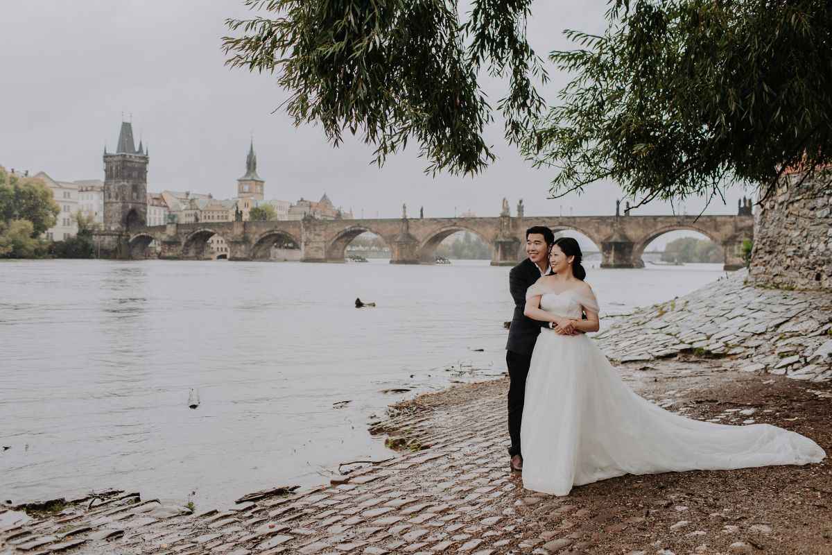 Pre-wedding photoshoot of a couple walking along the Vltava River with Prague Castle in the background
